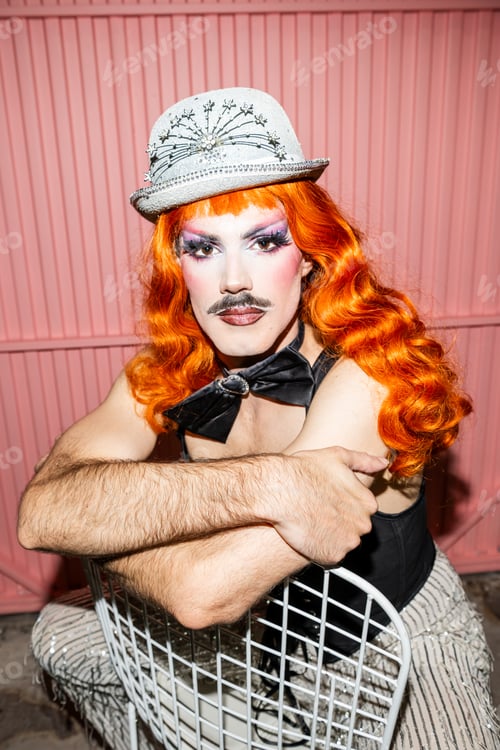 Preview: Queer Man With Orange Hair in Sparkling Hat Poses Confidently for Photo in Colorful Setting