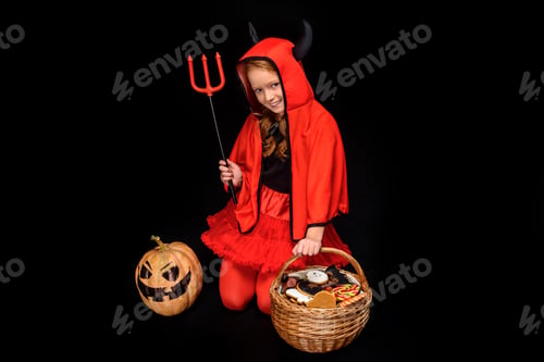 Preview: child in halloween costume of devil with pitchfork, jack o lantern and sweets in basket, isolated on
