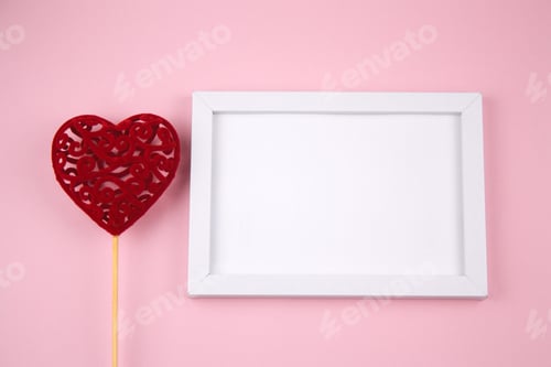 Preview: empty white wooden frame and red heart on a pastel pink background