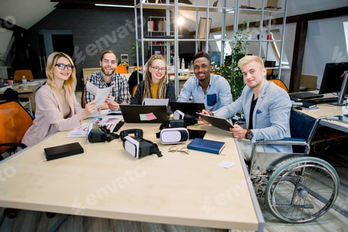 Preview: Creative team of diverse business people sitting at office table during meeting, looking at camera