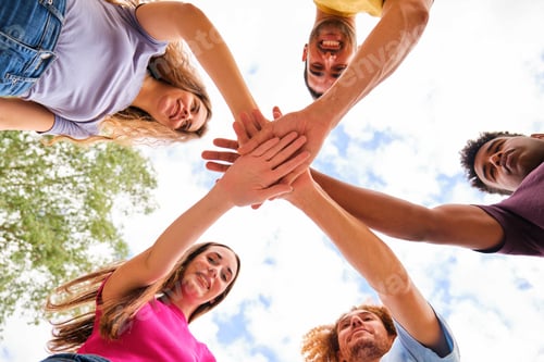 Preview: Low angle view of multiracial friends stacking hand together at street.