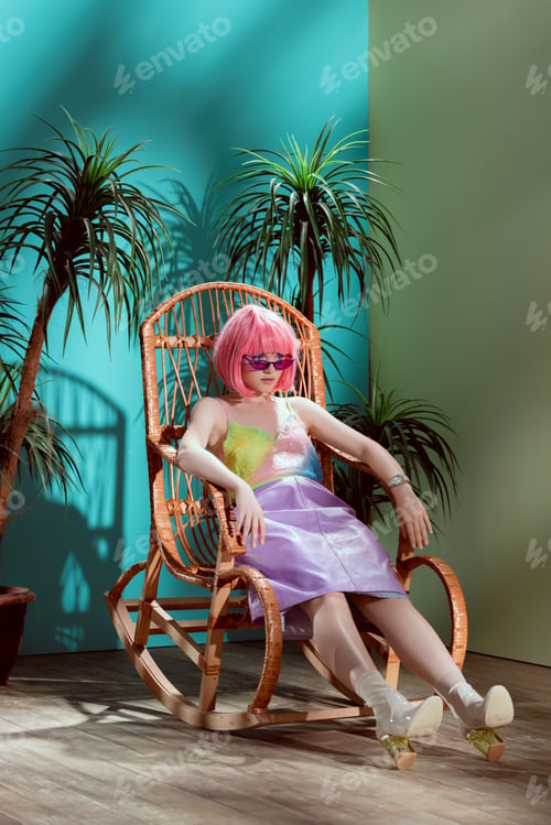 Preview: full length view of beautiful fashionable young woman sitting on rocking chair and looking away