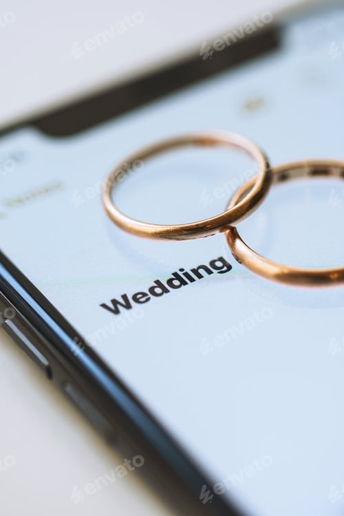 Preview: Golden wedding rings on top of a smartphone and the text on the screen - Wedding