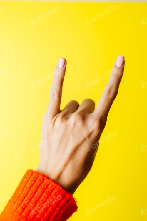 Preview: Woman's hand in red sweater shows rockstar gesture on yellow background