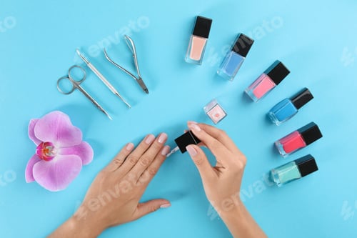 Preview: Woman applying nail polish on color background, above view