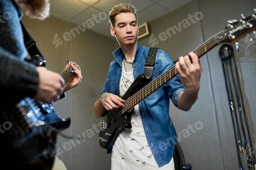 Preview: Concentrated musician playing guitar with mentor in studio