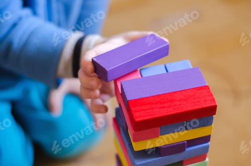 Preview: A child plays a game of wooden colored blocks jenga, close-up, selective focus