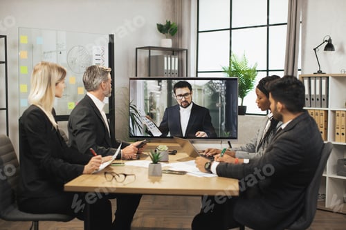 Preview: Focus on handsome bearded businessman in formal suit showing statistics charts from huge TV screen.