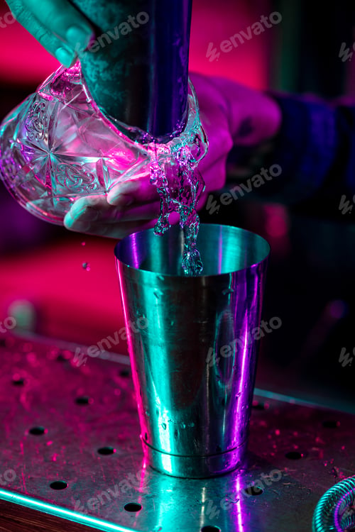 Preview: Close up of barman finishes preparation of alcoholic cocktail, pouring drink in multicolored neon