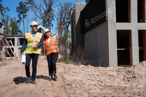 Preview: Building engineer and foreman with blueprint walking along construction site