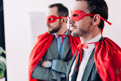 Preview: serious handsome super businessmen in masks and capes looking away in office