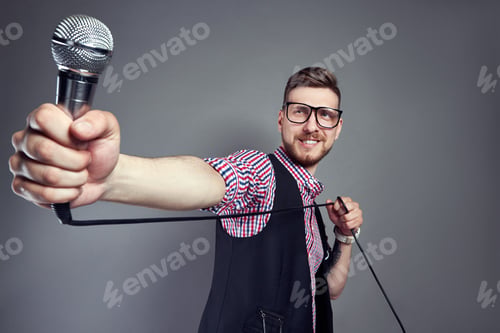 Preview: Karaoke man sings the song to microphone, singer with beard on grey background. Funny man in glasses