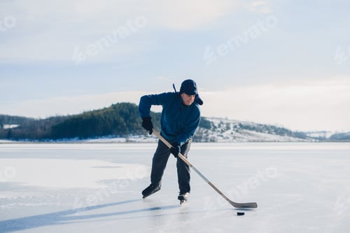Preview: An elderly man practices stricking the puck with hockey sticks on a frozen lake in winter.
