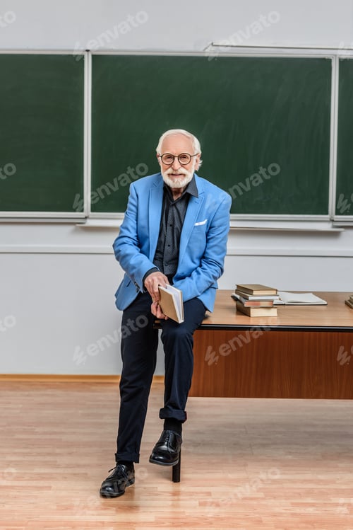 Preview: grey hair professor sitting on table in lecture room and holding book