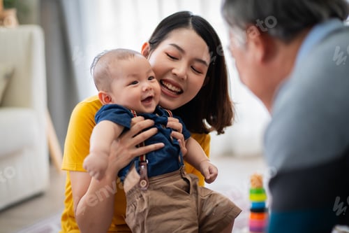 Preview: A man and a woman are playing with a baby in a living room. The baby is holding a toy and smiling.