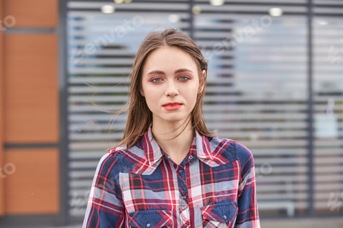 Preview: Young caucasian female in plaid shirt standing outdoors near modern building
