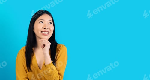 Preview: Curious young asian woman looking at copy space on blue
