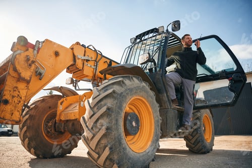 Preview: View from below, using walkie talkie. Man is with tractor. Agricultural worker