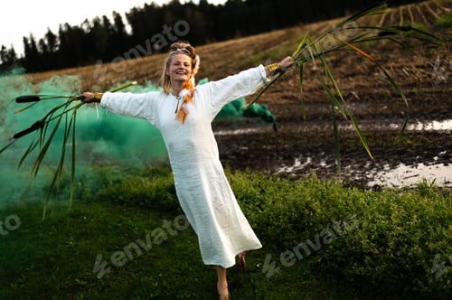 Preview: Happy woman in white dress with green smoke bomb dancing on muddy field, freedom and emotions