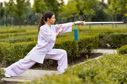 Preview: Caucasian woman working out with Tai Chi sword in the morning at the park