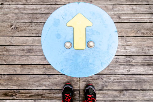 Preview: Arrow indicating direction with traveler's feet on a wooden background.