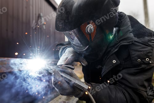 Preview: Welder man welding metal iron with electrodes, worker wearing protective helmet and gloves