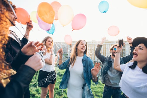 Preview: Group of friends enjoying roof party, holding helium balloons