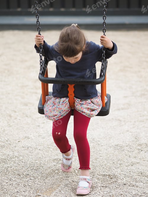 Preview: Little cute stylish girl in brightly colored swings on a swing at the playground on a summer day