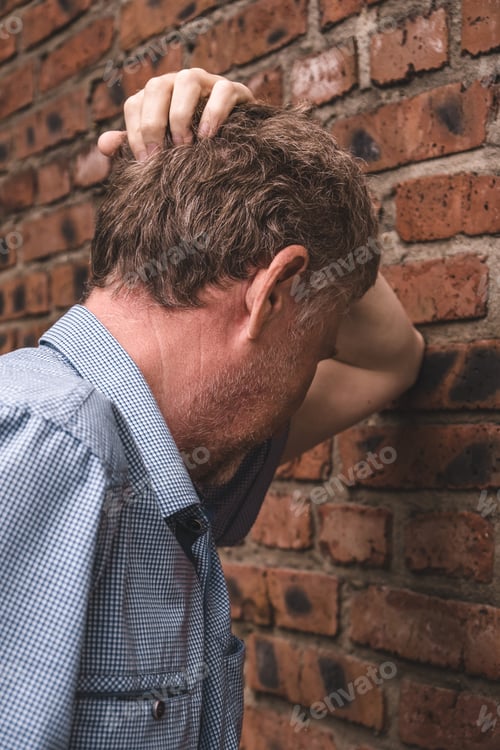 Preview: Candid portrait of frustrated man in depression,near brick wall on the street. Psychological problem