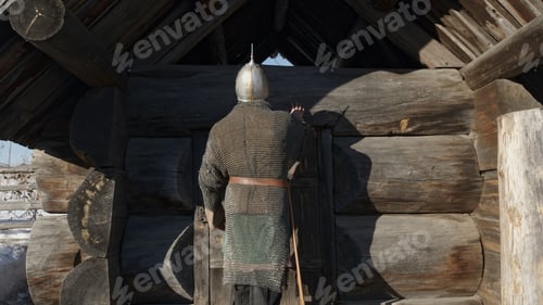 Preview: A medieval warrior in chain armor and a sword coming to wooden house. Media. Strong ancient warrior.