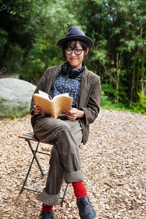 Preview: Japanese woman wearing glasses and hat sitting on chair outside Eco Cafe, reading book.