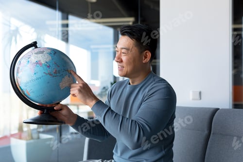 Preview: Asian male blogger tourist, looking at camera and smiling holding globe