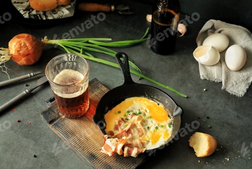 Preview: Fried eggs with bacon in a frying pan on the table, beer and other food products for lunch