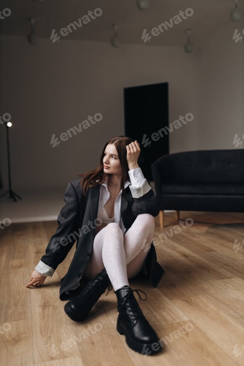 Preview: Pretty woman with a square haircut in a black jacket sitting on the floor. Stylish young woman
