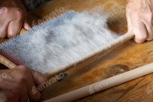 Preview: hands removing carded raw wool from a carding board with a round stick, on wooden surface
