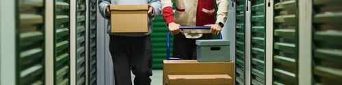 Preview: Middle Aged Man and Young Adult Man Transporting Boxes down Storage Aisle