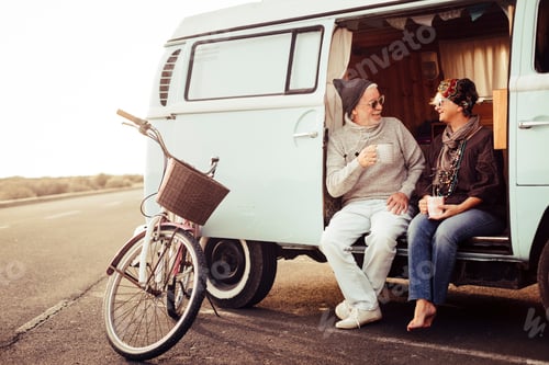 Preview: Adult aged caucasian happy couple sit down out of a vintage van drinking a tea and trave