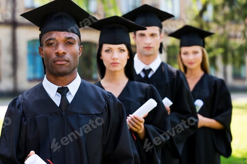 Preview: Feeling confident about their future. Four college graduates standing in a row and looking at camera