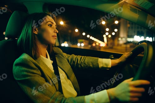 Preview: Young pensive woman driving car through the city at night.