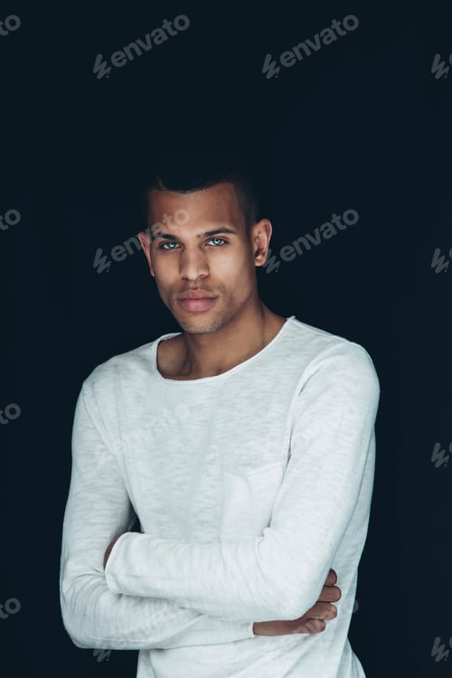 Preview: Portrait of young man with crossed arms wearing white sweatshirt in front of black background