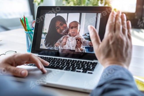 Preview: Man waving and speaking on video call with his wife and baby daughter on laptop in the office.