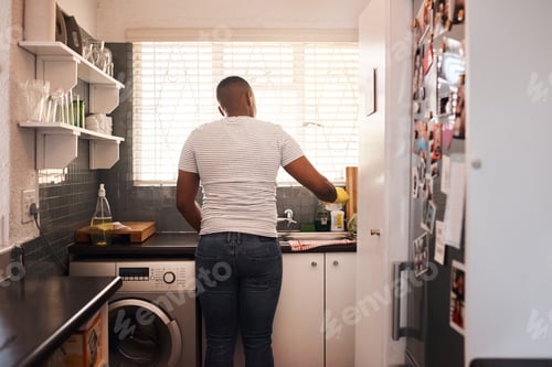 Preview: A clean kitchen is better than a dirty one. Rearview shot of a man doing the dishes at home.
