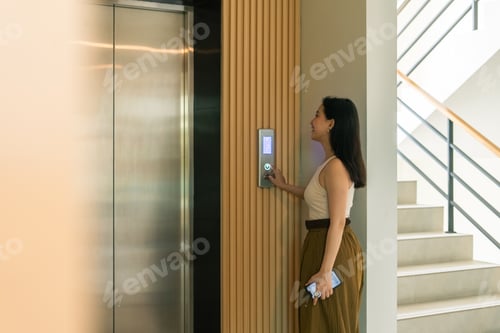 Preview: Woman pressing elevator button, waiting in modern building for daily commute