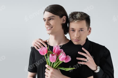 Preview: Young gay embracing boyfriend with tulip flowers isolated on grey
