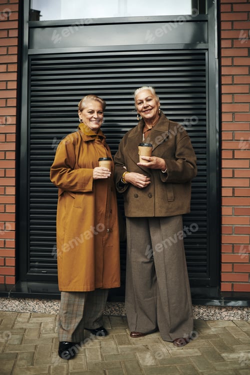 Preview: Senior Women Standing Outdoors Holding Coffee Cups Smiling Together