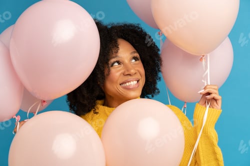 Preview: Happy dark skinned woman among pastel pink air balloons with joy and happiness, celebrates birthday