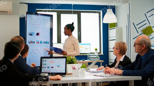 Preview: Black woman worker explaning company statistics in front of colleagues