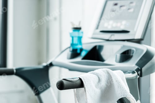 Preview: selective focus of white towel hanging on modern treadmill in gym