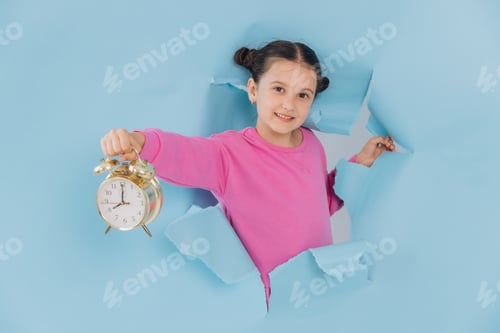 Preview: Little girl looking out of a torn hole in a blue paper and showing a clock, discount time