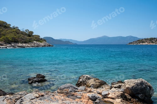 Preview: Greece Aponisos beach Agistri island. Rocky land, pine tree, clear sea water, blue sky background.